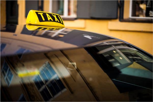 A taxi with a roof sign is parked on a street, reflecting the surrounding buildings, much like a Philadelphia Uber accident lawyer navigating the complex urban landscape.