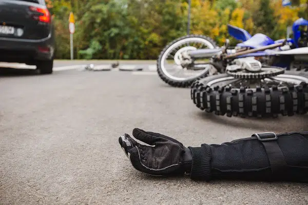 A Philadelphia motorcycle accident scene is marked by a fallen bike on the road, with a car nearby and the gloved hand of a person lying still on the ground.