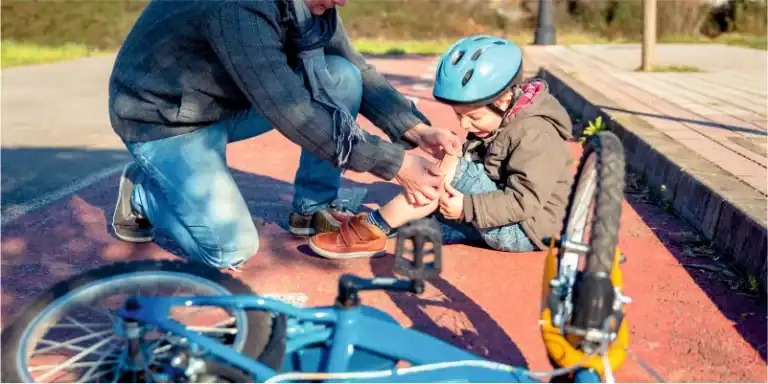 An adult comforts a child with a scraped knee from a bicycle fall on a paved path, the bike resting nearby. Just as Bristol Child Injury Attorneys advocate for young ones' well-being, the adult provides care and reassurance in this moment of need.