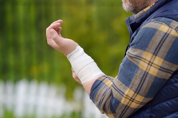 A person wearing a plaid shirt and vest holds their bandaged wrist outside, perhaps considering contacting a Bucks County personal injury lawyer.