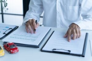 Businessman signing car insurance document beside toy car and calculator on desk