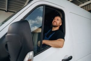Smiling courier seated in delivery van holding cardboard box