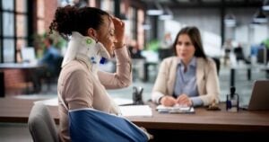 Woman wearing neck brace and arm sling seated across desk from attorney