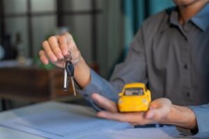 attorney holding car keys and toy car model over documents on desk