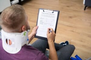 injured person wearing neck brace completing Health Insurance Claim Form on clipboard