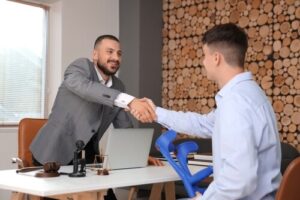 male lawyer shaking hands with injured client holding crutches in office